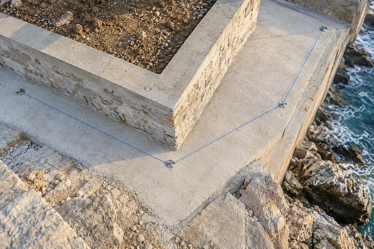 Generated editorial image of four metal markers joined by three blue layout strings along a coastal retaining structure