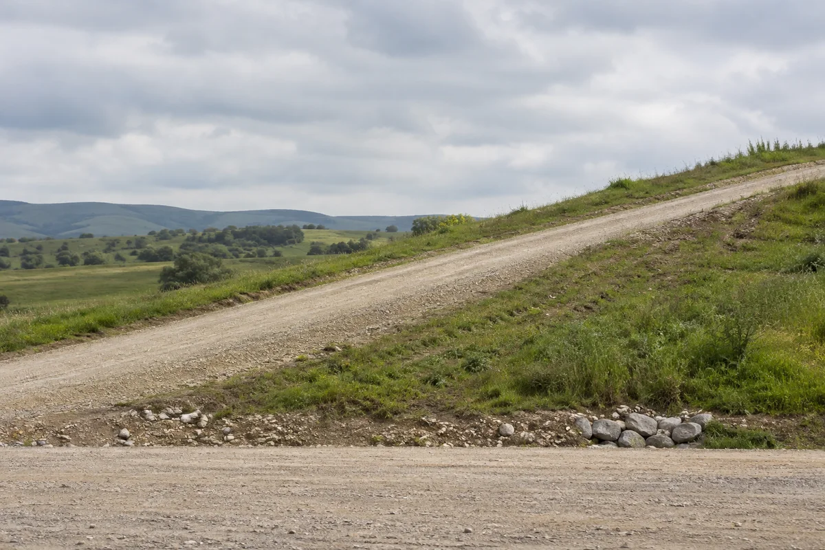 A gravel access road climbing across a grassy embankment