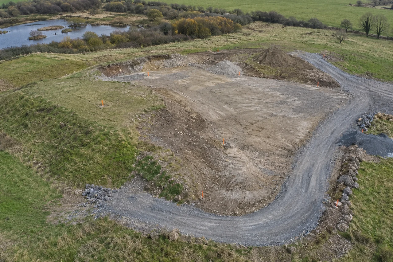 Generated editorial aerial photograph of an earthworks site with survey markers around a gravel access track